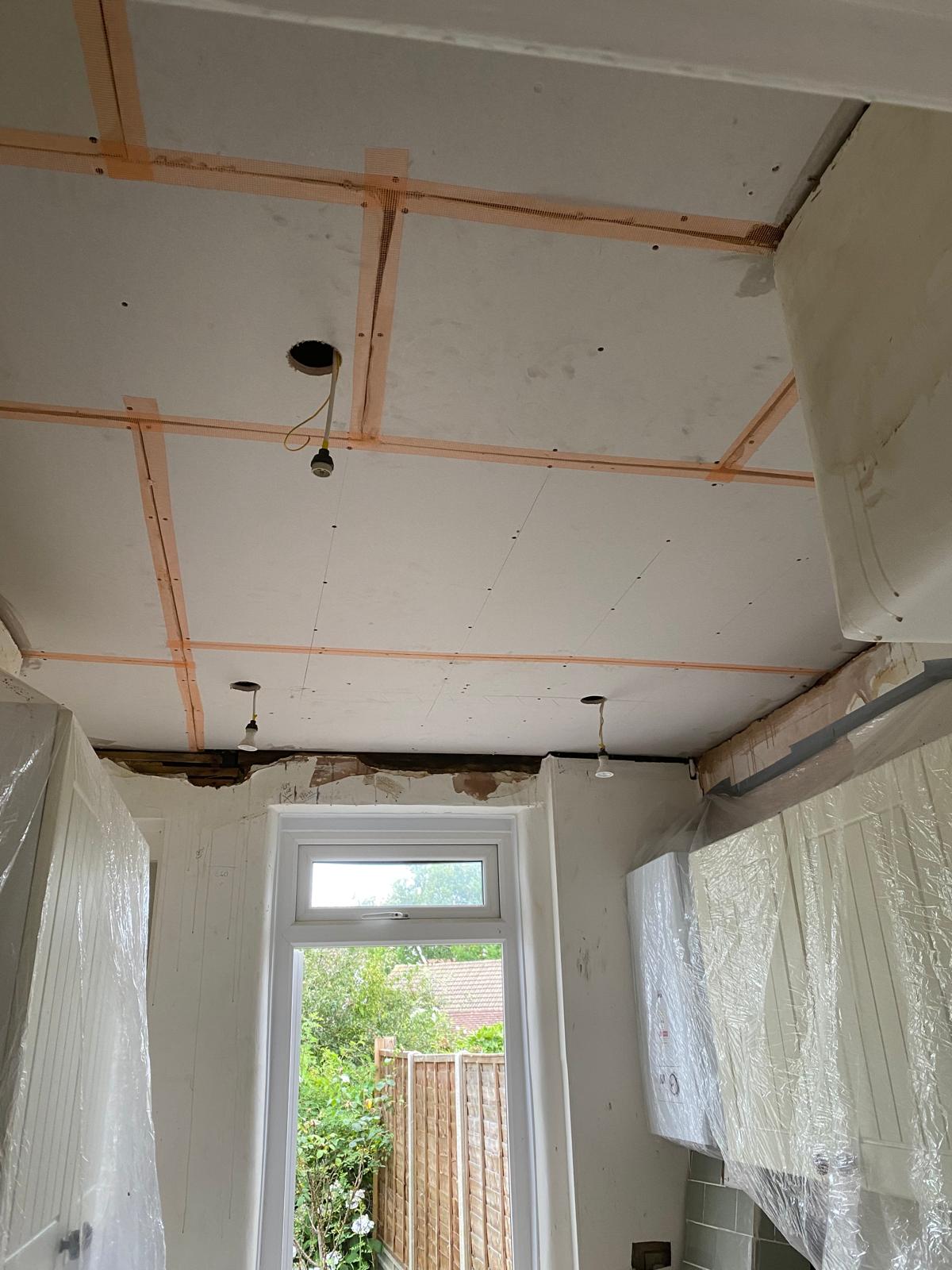 New moisture-resistant plasterboard fixed to ceiling joists with scrim tape at joints, kitchen in Epsom