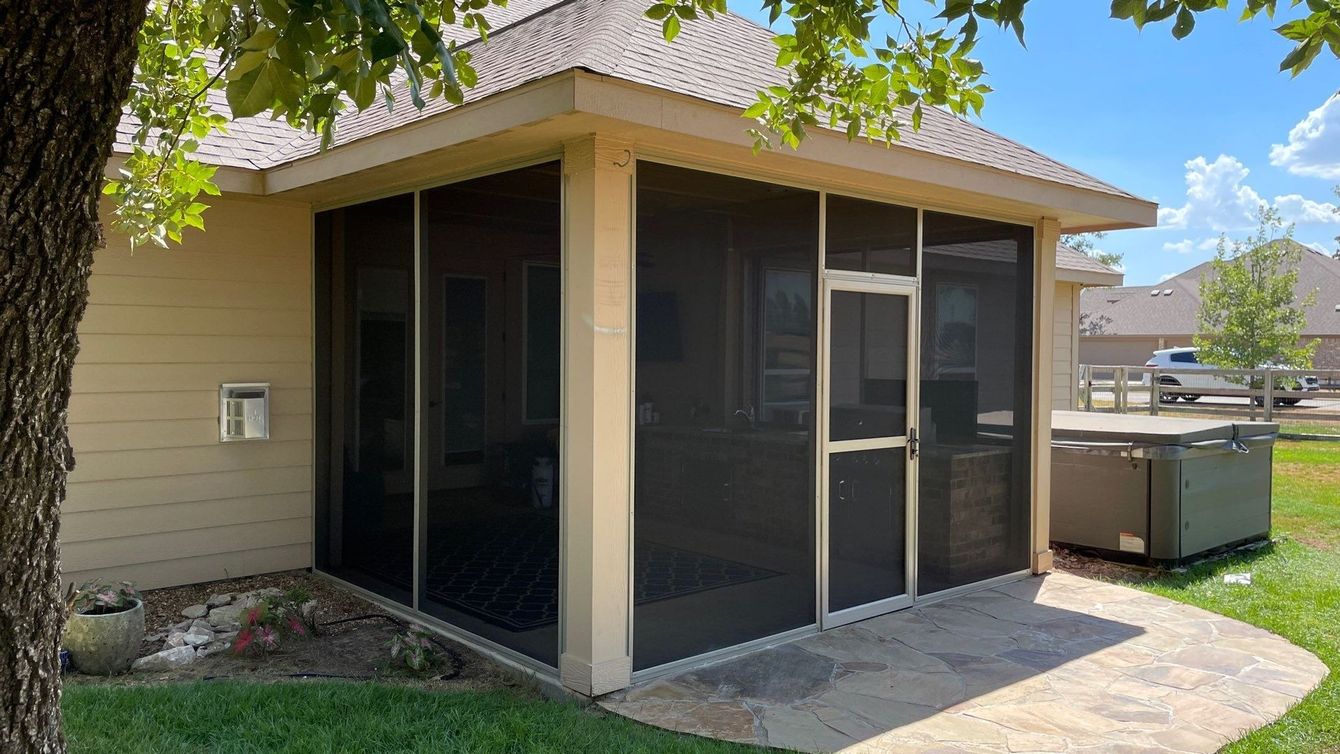 Screened-in patio enclosure with dark screens attached to a beige home