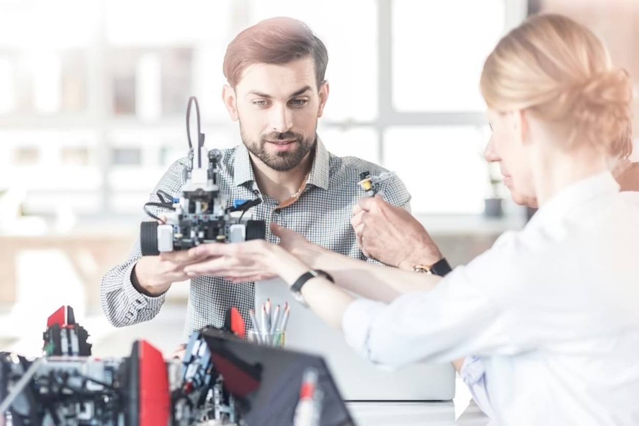 A tech team sits at a table working on a mechanical prototype.
