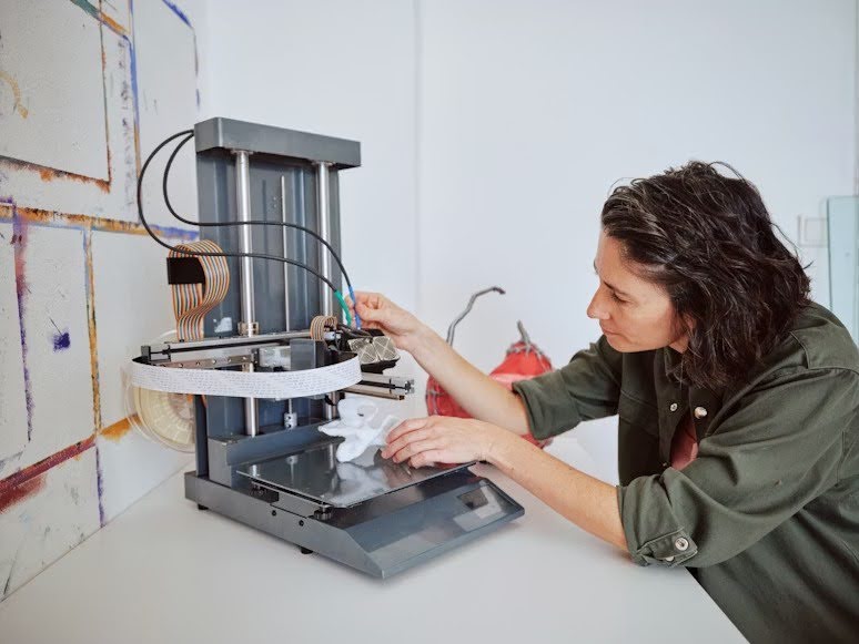 A woman creating a white star-shaped product using a 3D printer