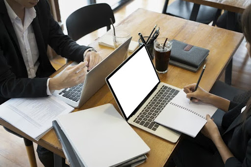 Two office workers are reviewing documents on their laptops. Two office workers are reviewing documents on their laptops.