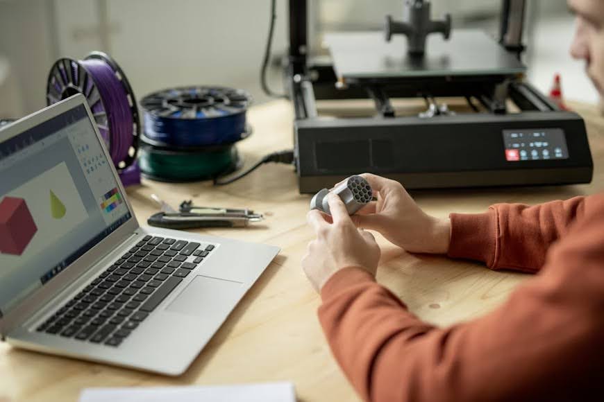 Hands of a young male engineer holding a prototype over a wooden table while sitting in front of a laptop
