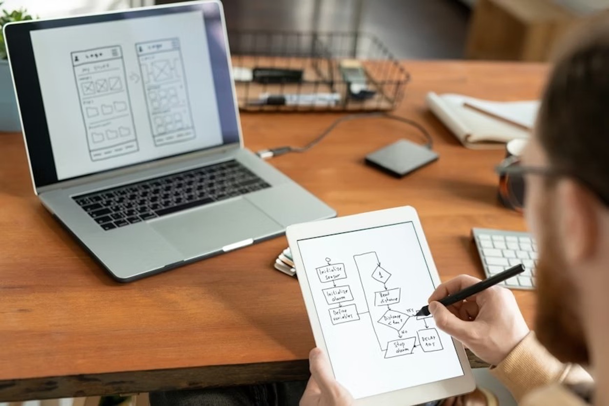 Over-shoulder view of a man using a digital tablet and a stylus and drawing a scheme for a prototype design