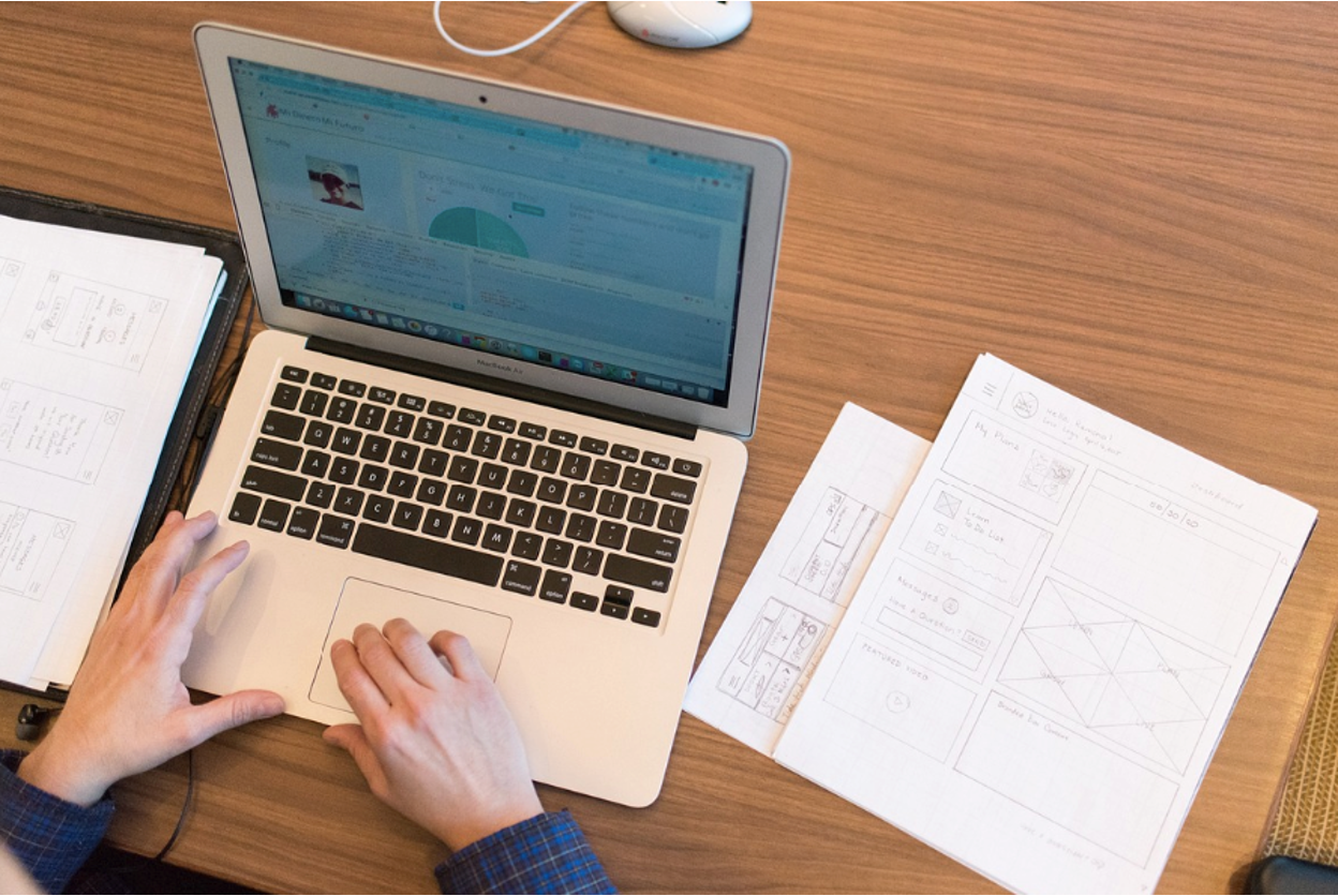 An inventor working on a computer, with design patent drawings on the table.