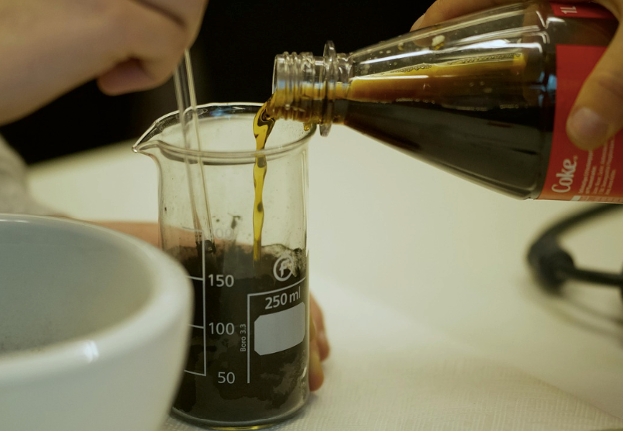 A person pouring Coca-Cola into a test cylinder