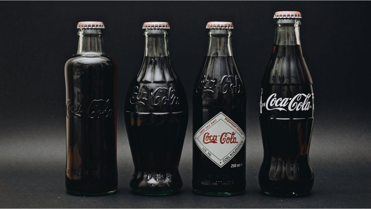 Different Coca-Cola glass bottles on a gray background showing the evolution of its design Different Coca-Cola glass bottles on a gray background showing the evolution of its design