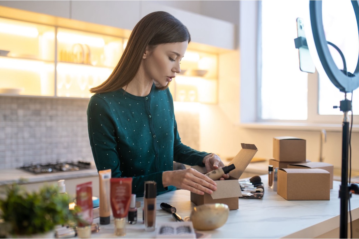 Young woman packing some products in front of a ring light and smartphone setup Young woman packing some products in front of a ring light and smartphone setup
