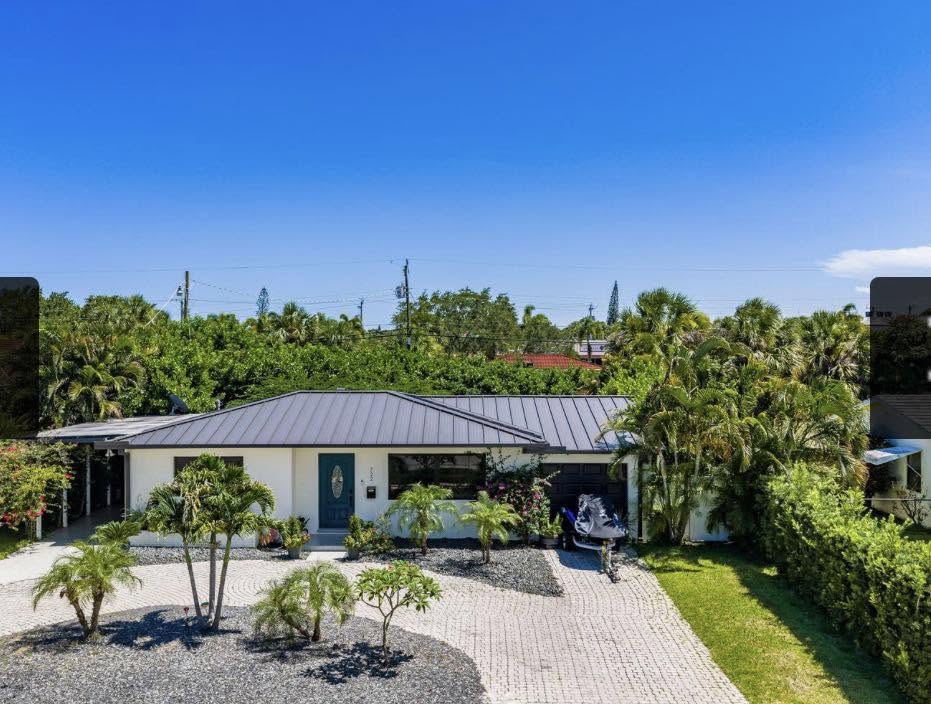 Aerial view of a modern white single-family home with a metal roof and paver driveway in Palm Beach County