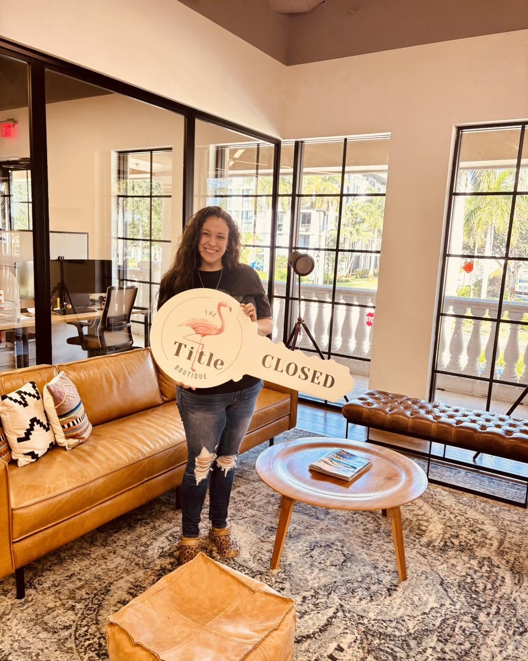 A client in The Title Boutique lobby holding the oversized wooden Title Closed key