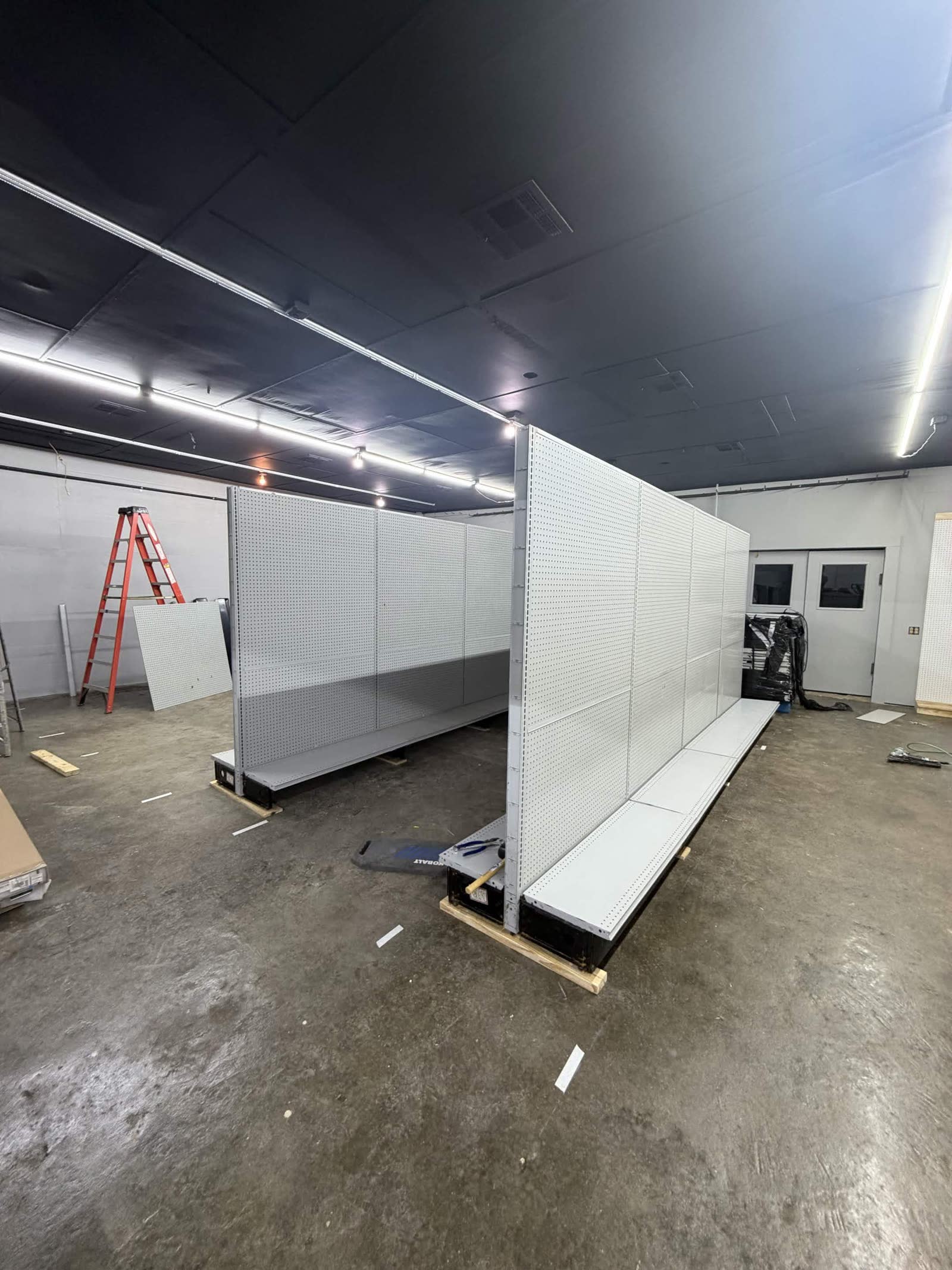 Fixtures phase — white pegboard shelving units being assembled and put in place mid-floor