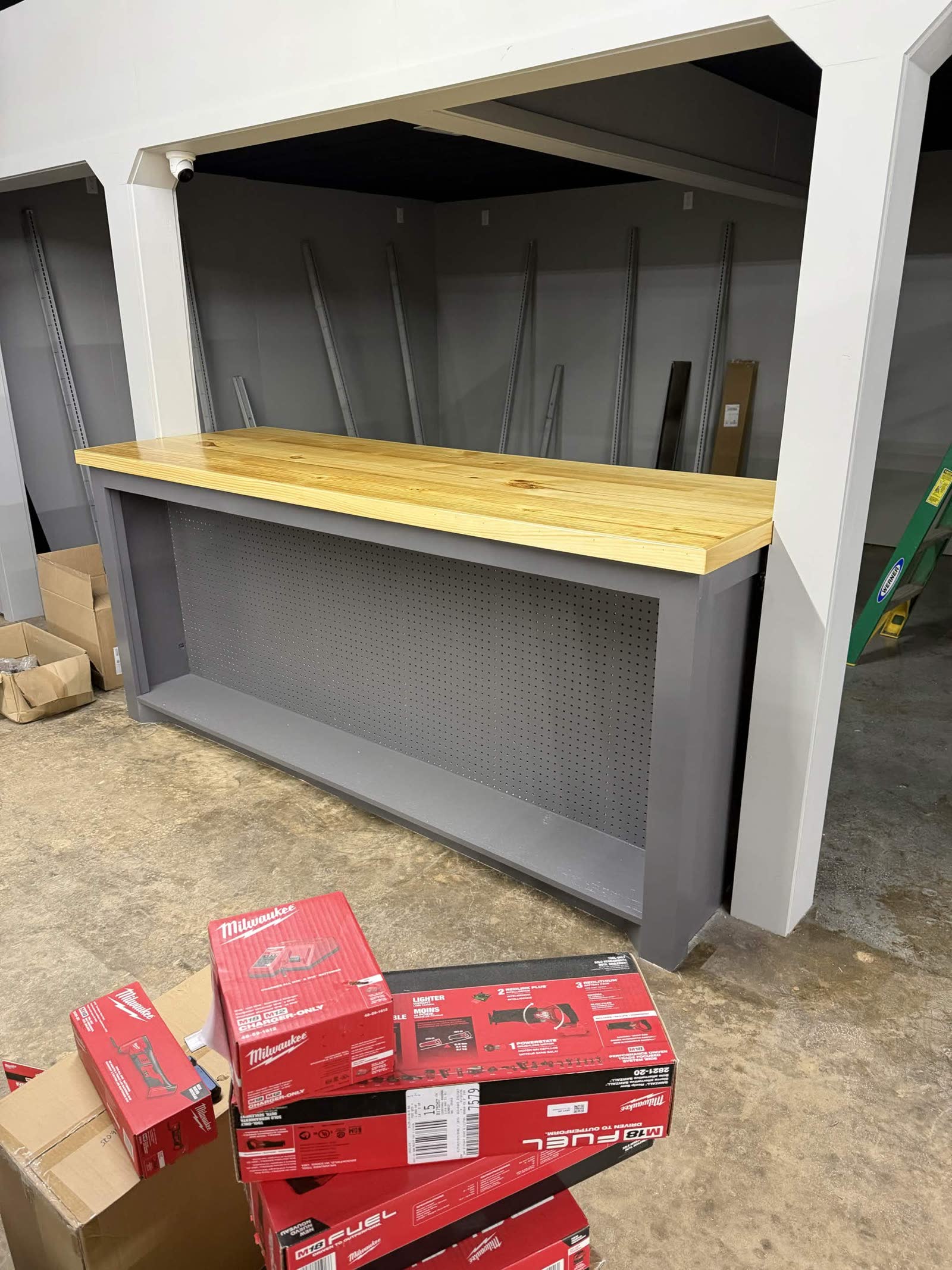 Counter finished — butcher block top in place, gray cabinet, Milwaukee M12 Fuel boxes stacked in the foreground waiting to be merchandised