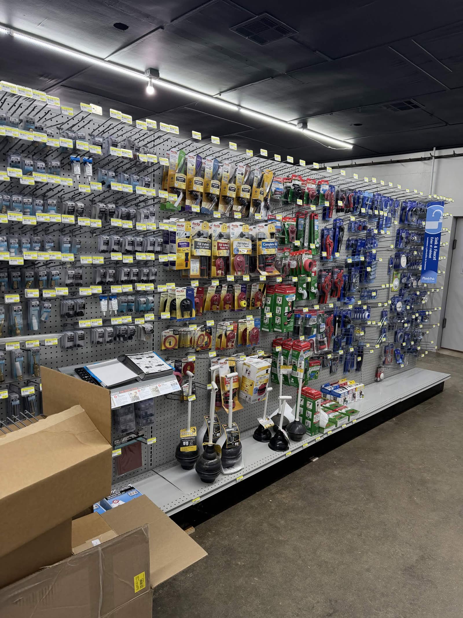 Stocking phase — plumbing aisle fully merchandised with toilet plungers, plumbing tools, and packaged blue items