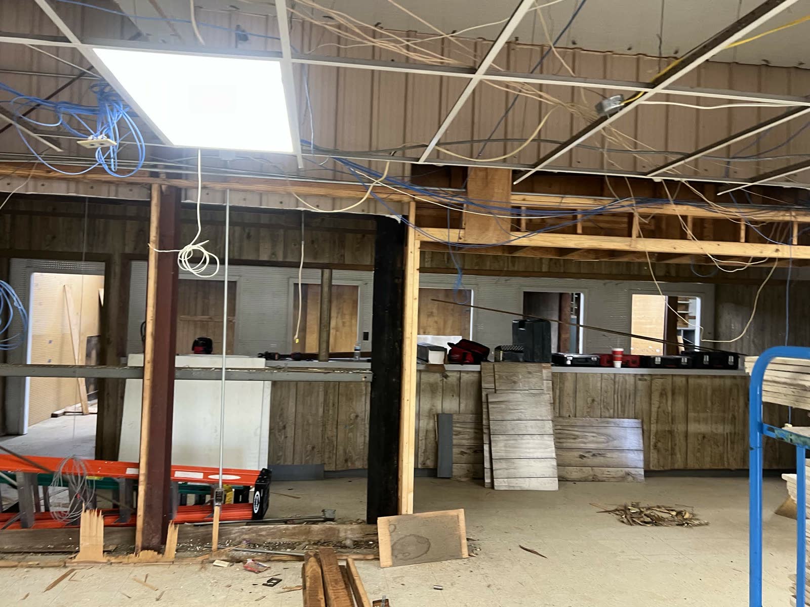Demo phase — exposed structural posts (one painted black, one wood) with wiring everywhere and a ladder mid-room
