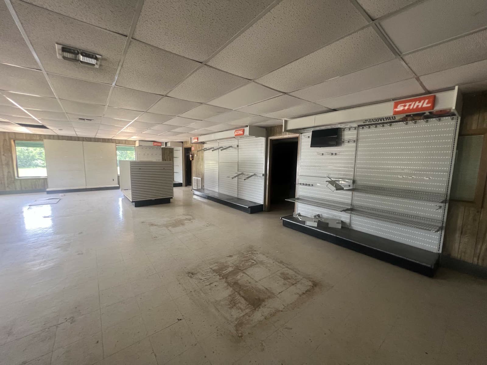 Cleared-out retail interior with drop ceiling, dirty floor, and a leftover STIHL pegboard sign on the back wall during the early build-out