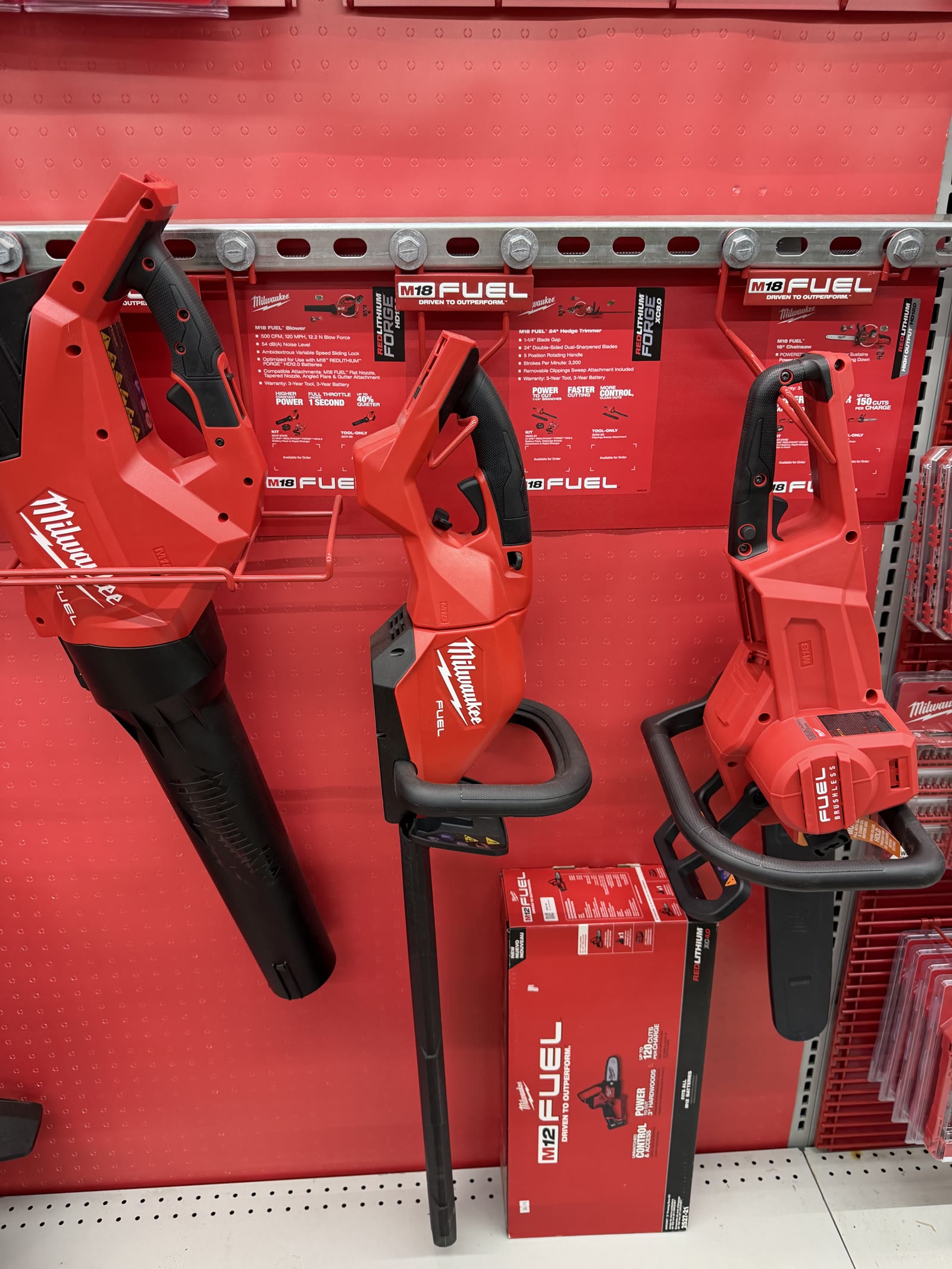 Milwaukee M18 FUEL outdoor power display — blower, hedge trimmer, and chainsaw on the red wall at Cardinal Hardware
