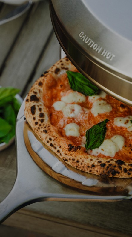Stone-baked margherita pizza sliding out of a Solo Stove Pi oven