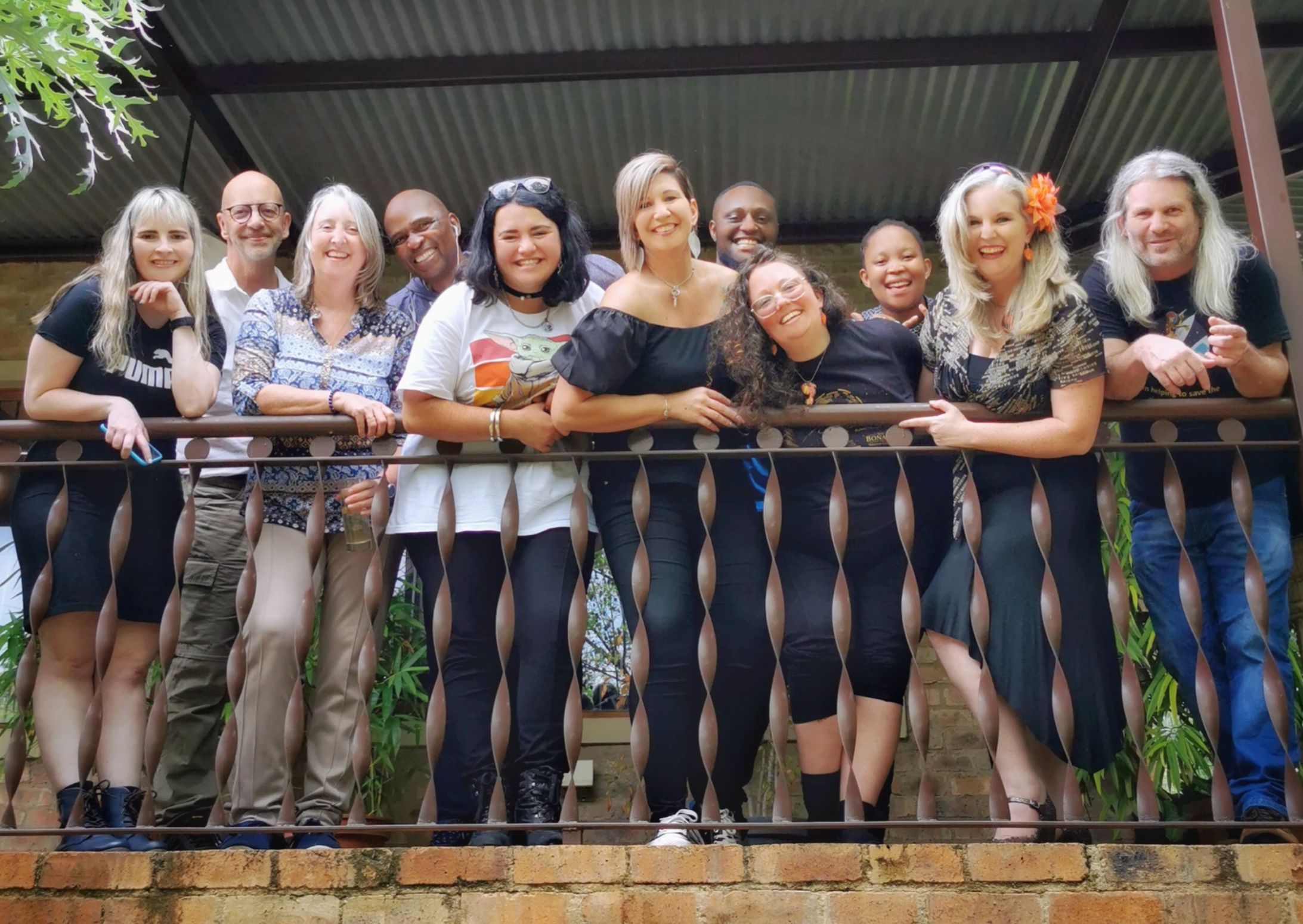 photo of a group of people standing on a balcony with wood and iron railings. overlooking greenery and plants.