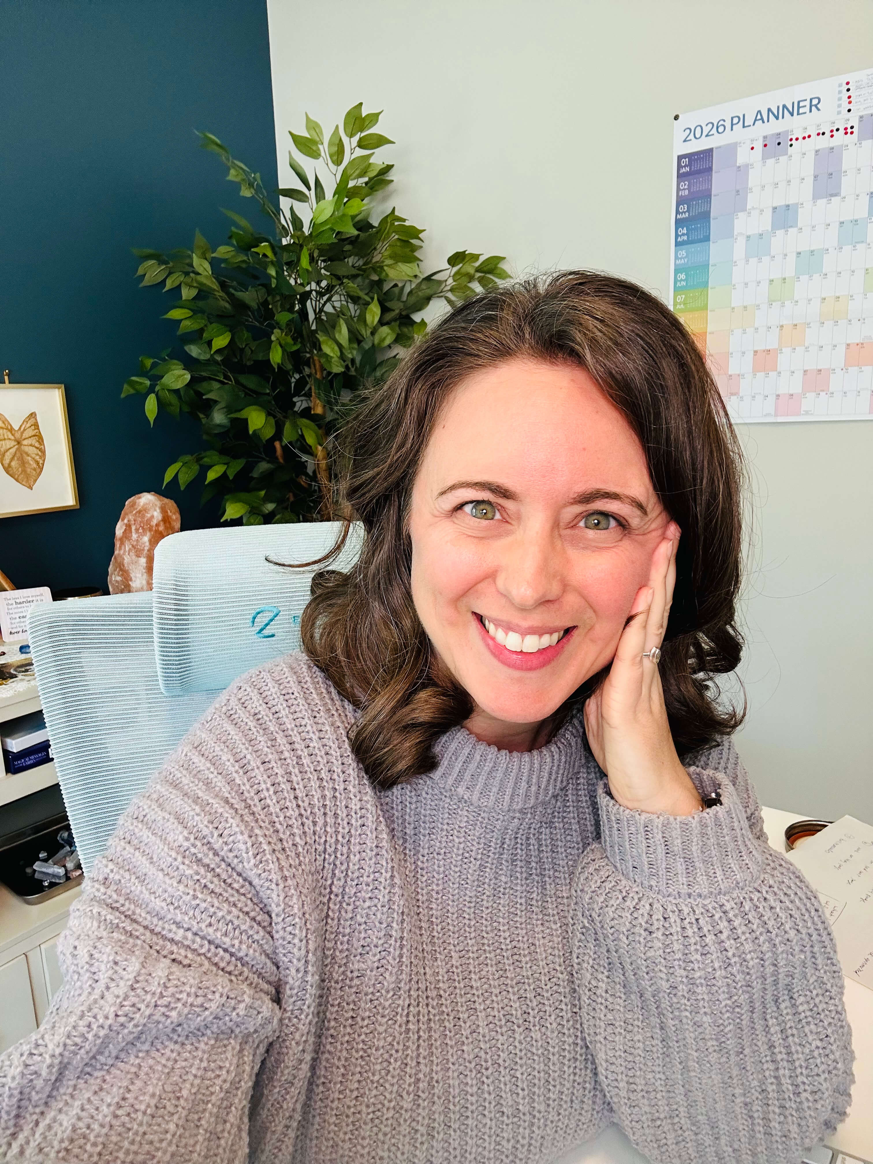 Chelsea Fournier, creator of Decide with Chelsea & curator of adulting resources, smiling at her desk wearing a grey sweater