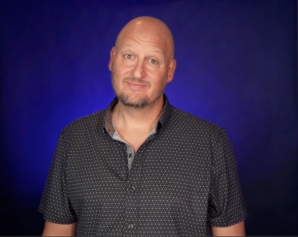 Todd Wall in a dark shirt against a blue studio backdrop