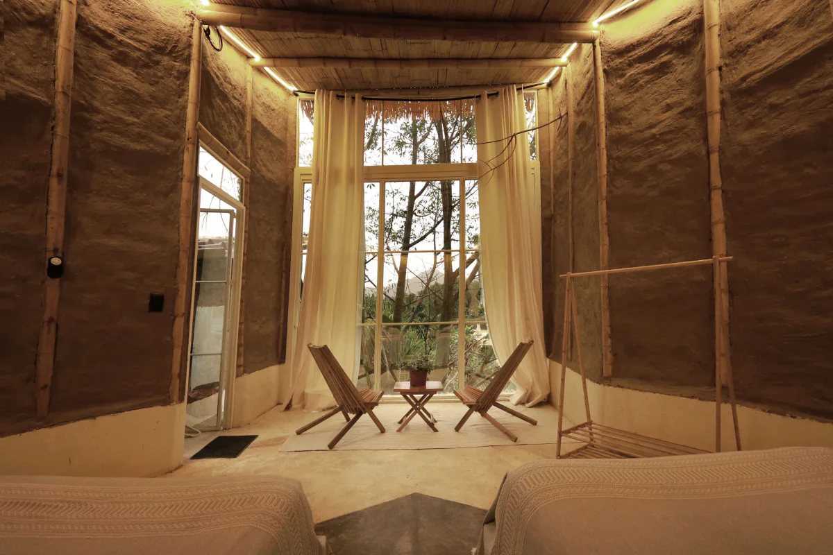 An earthen-wall guest room with full-height windows onto the forest at the Vādma Mexico training venue
