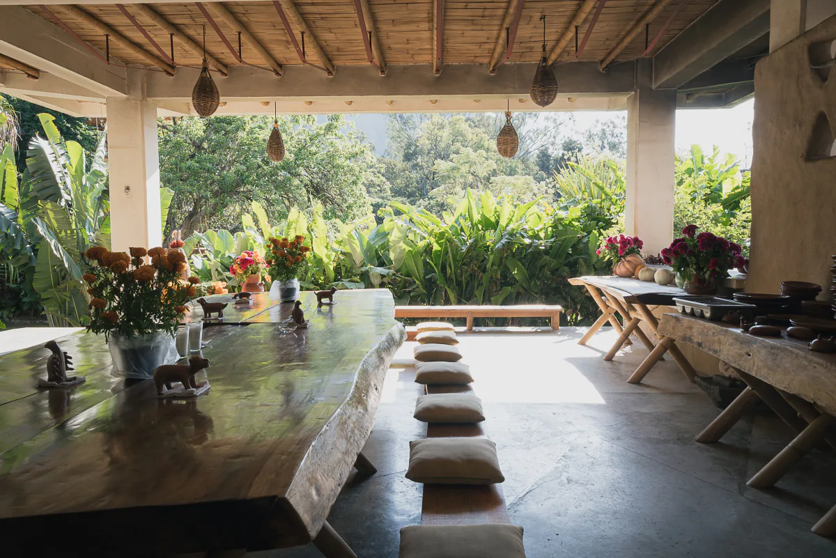 The open-air dining pavilion at the Vādma training venue near Mexico City, long wooden table set with marigolds under a bamboo roof