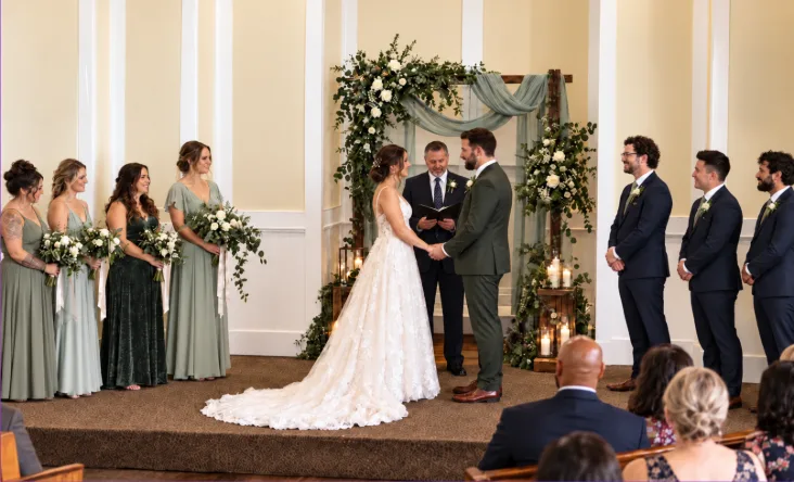 Wedding ceremony inside Madison Hill Chapel with the bride and groom at the floral arch surrounded by their wedding party and seated guests