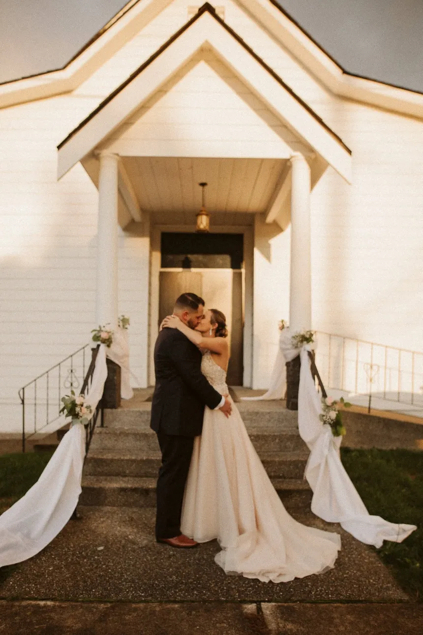 A real couple kissing at the entrance of Madison Hill Chapel, framed by the pointed-arch portico