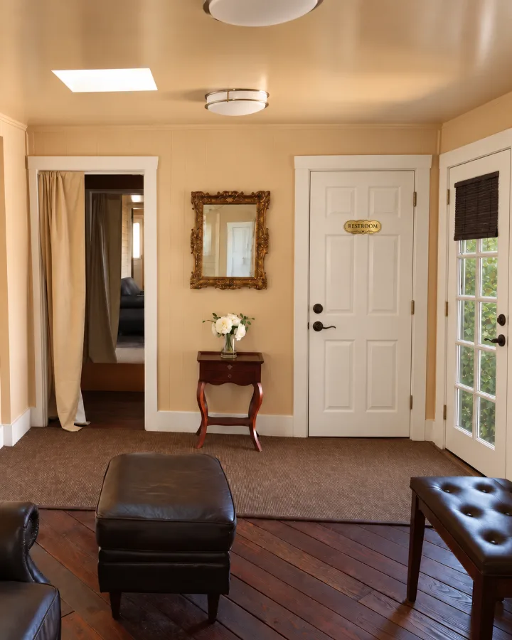 Madison Hill bridal suite with leather seating, gold framed mirror, side table with white flowers, and restroom