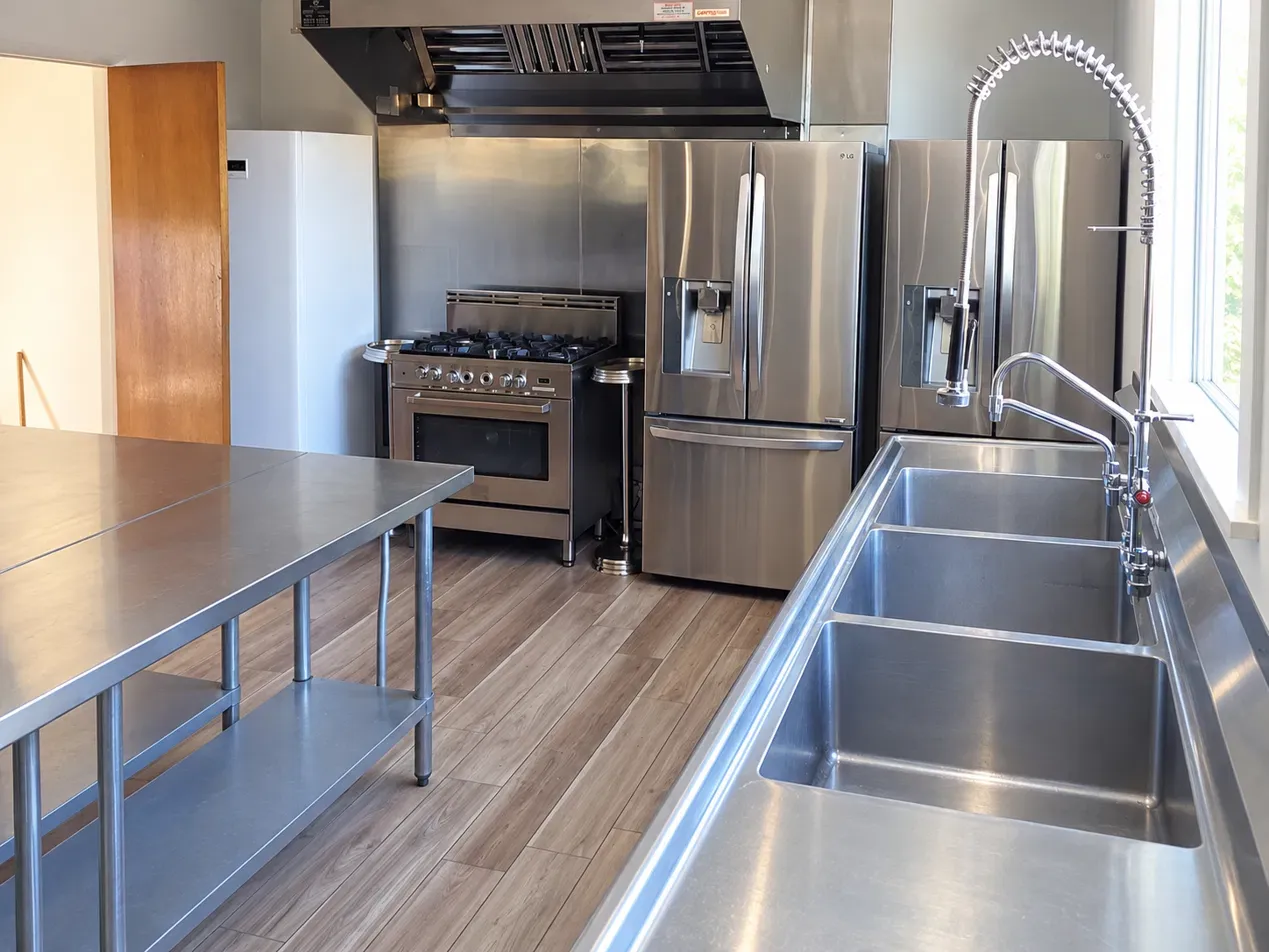 Madison Hill commercial kitchen with a stainless steel range, hood, refrigerator, and prep table