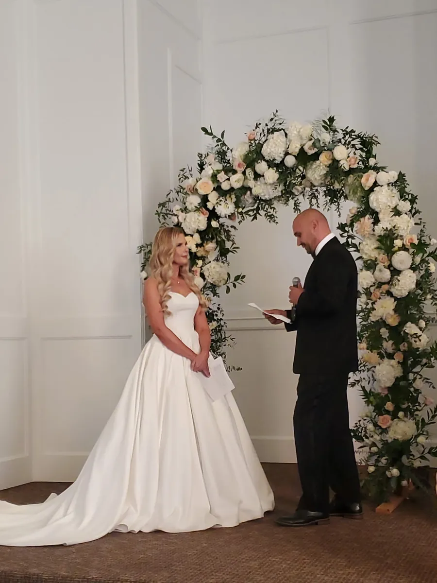 A bride and groom sharing their vows at the floral arch inside Madison Hill Chapel.