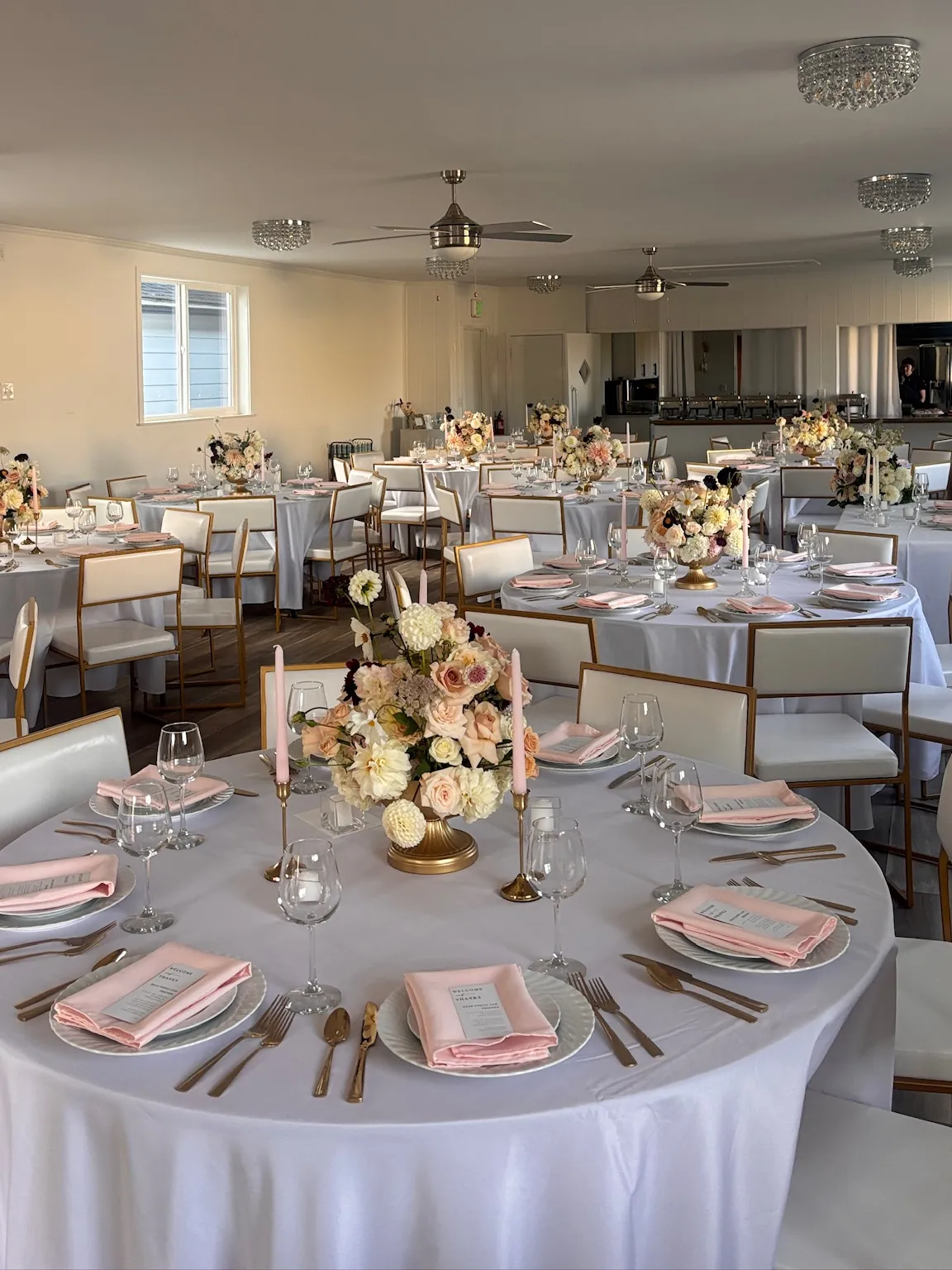Reception hall set with round tables, blush napkins, and gold chairs