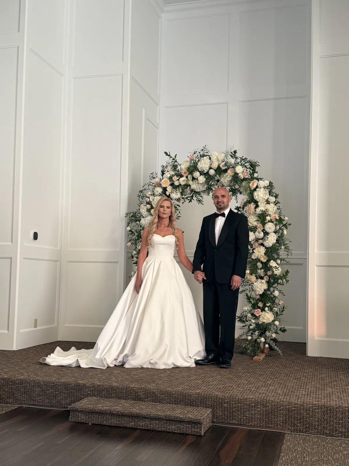 Bride and groom standing at the flower arch inside the chapel