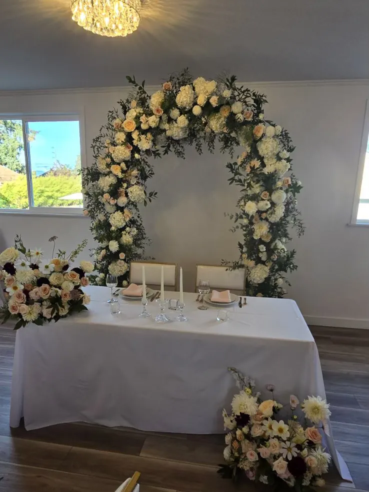 Sweetheart table with candles and a flower arch behind it