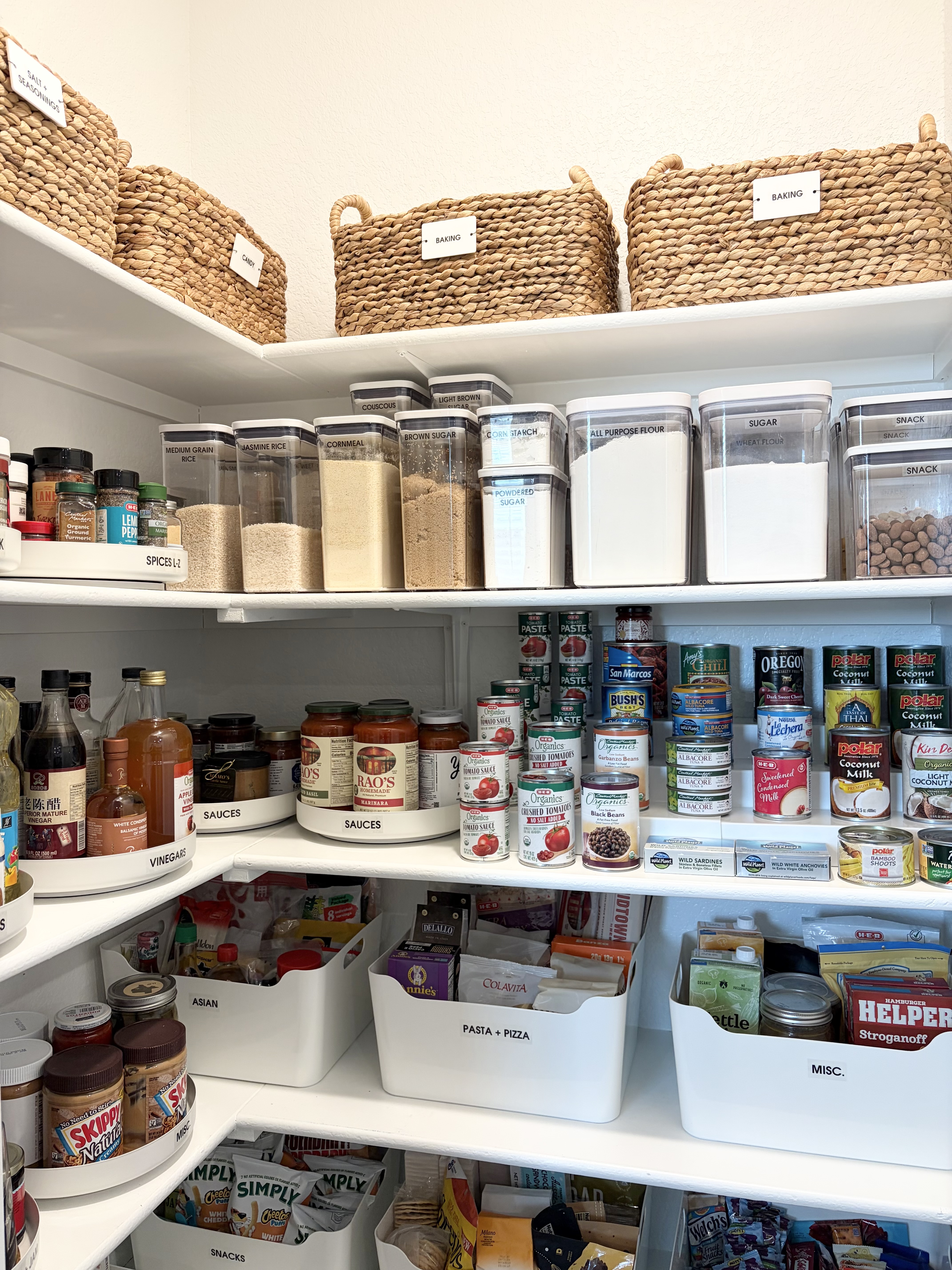 Corner pantry organized with Lazy Susans, labeled baskets, clear canisters, and white bins
