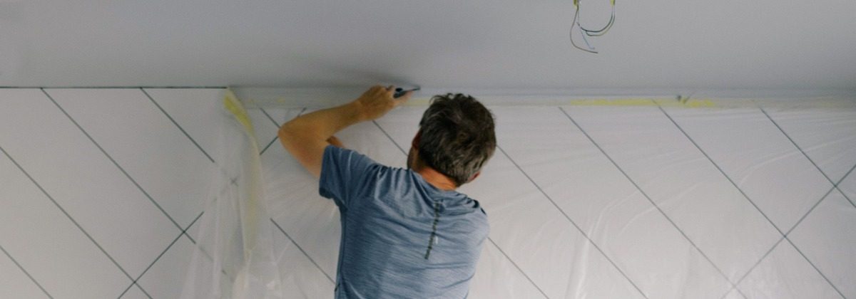 Painter cutting in along the ceiling of a room prepared for painting