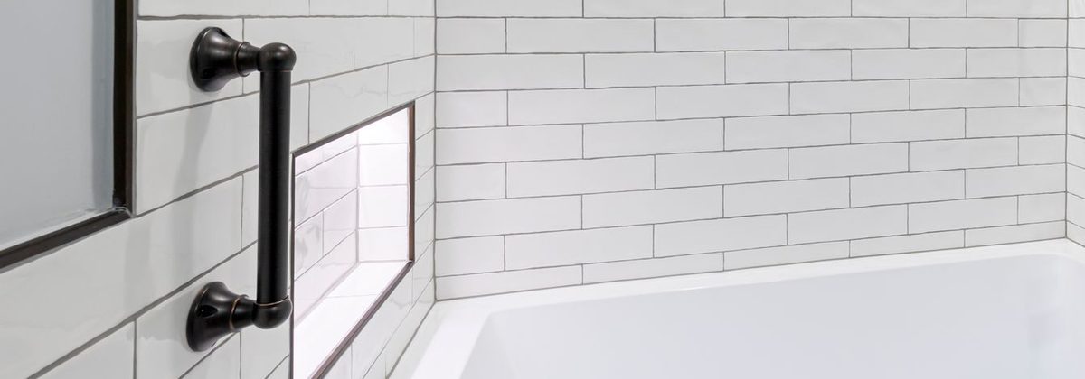 Dark bronze grab bar beside a bathtub in a white-tiled bathroom