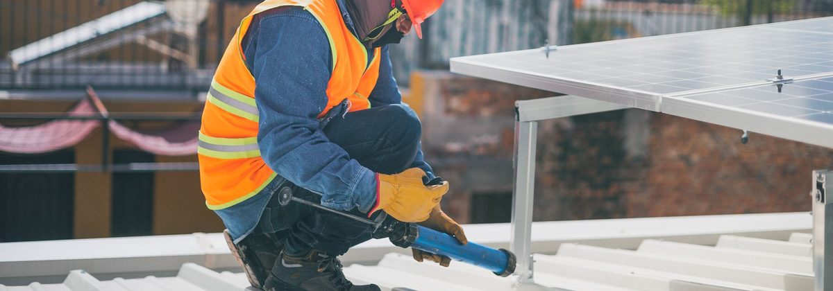 Worker applying sealant with a caulking gun on a metal roof