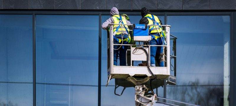 Two workers on a boom lift beside a commercial glass facade