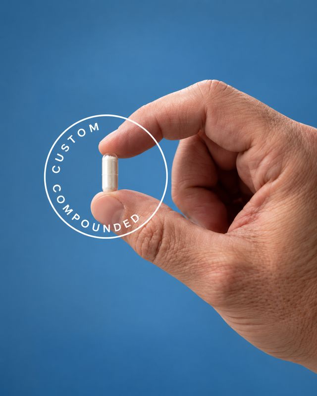 A hand holding one custom-compounded capsule