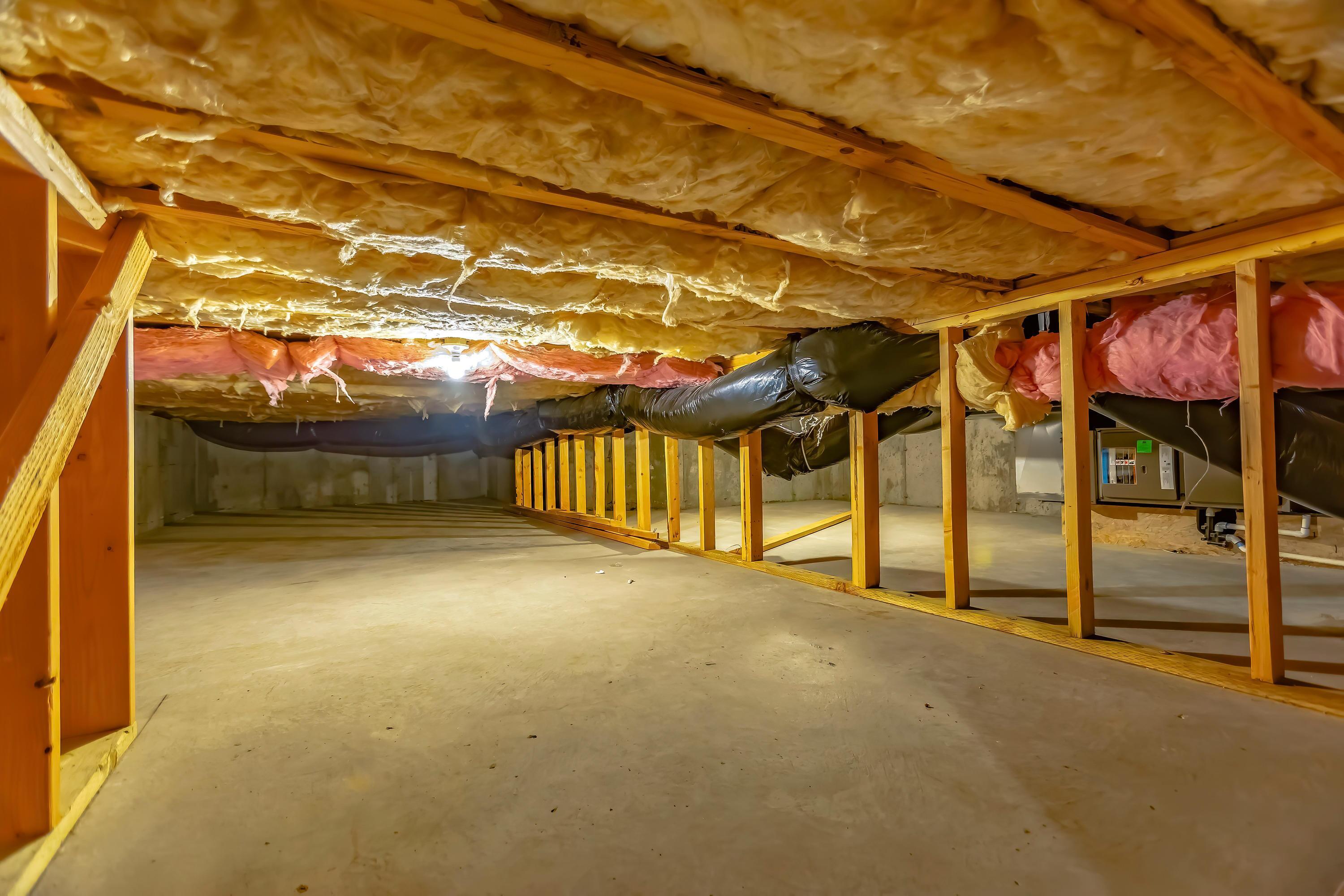 Wide crawl space showing insulation positioned between wooden floor joists.