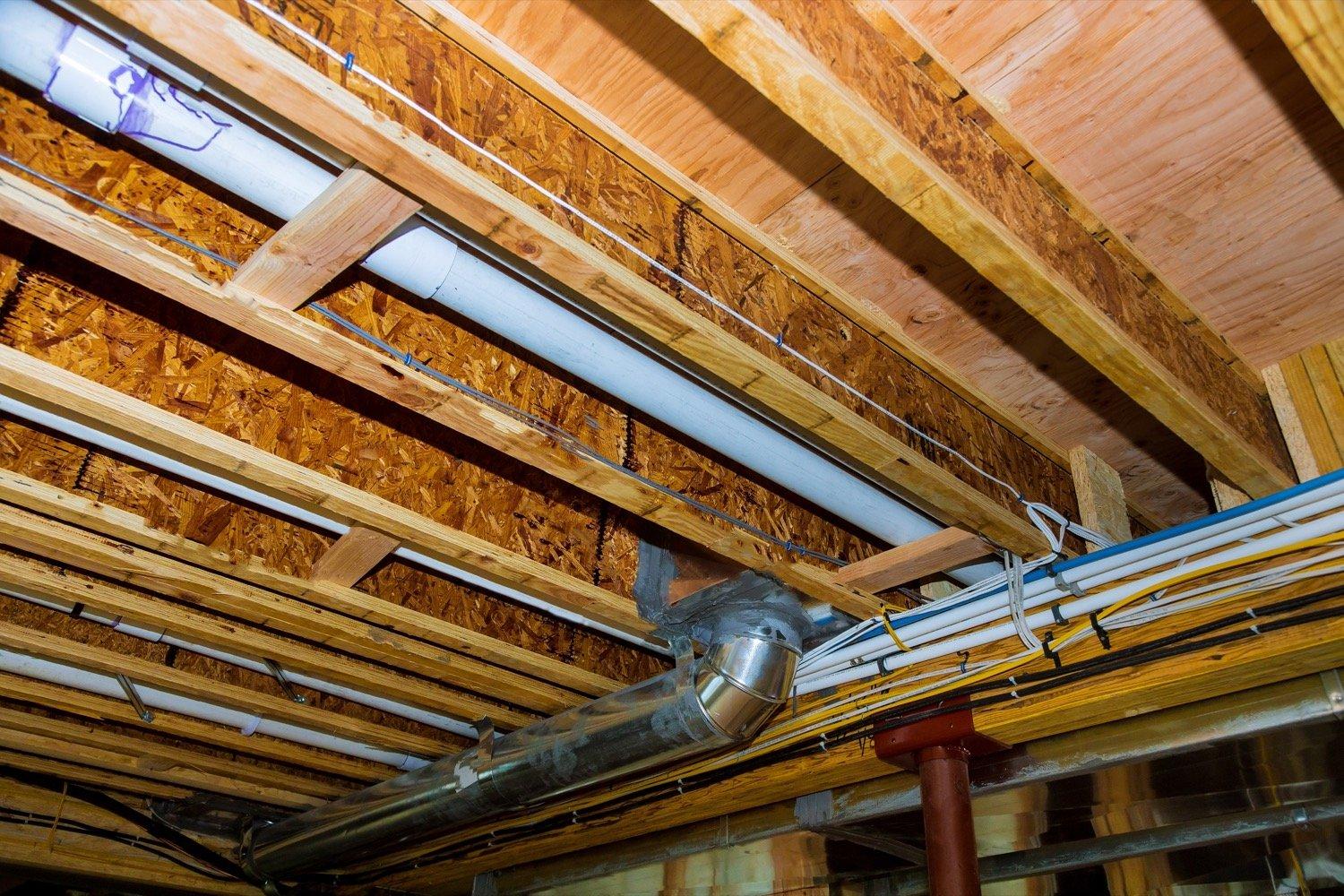 Crawl space containing framing, plumbing, and insulation from different stages of a home's history.