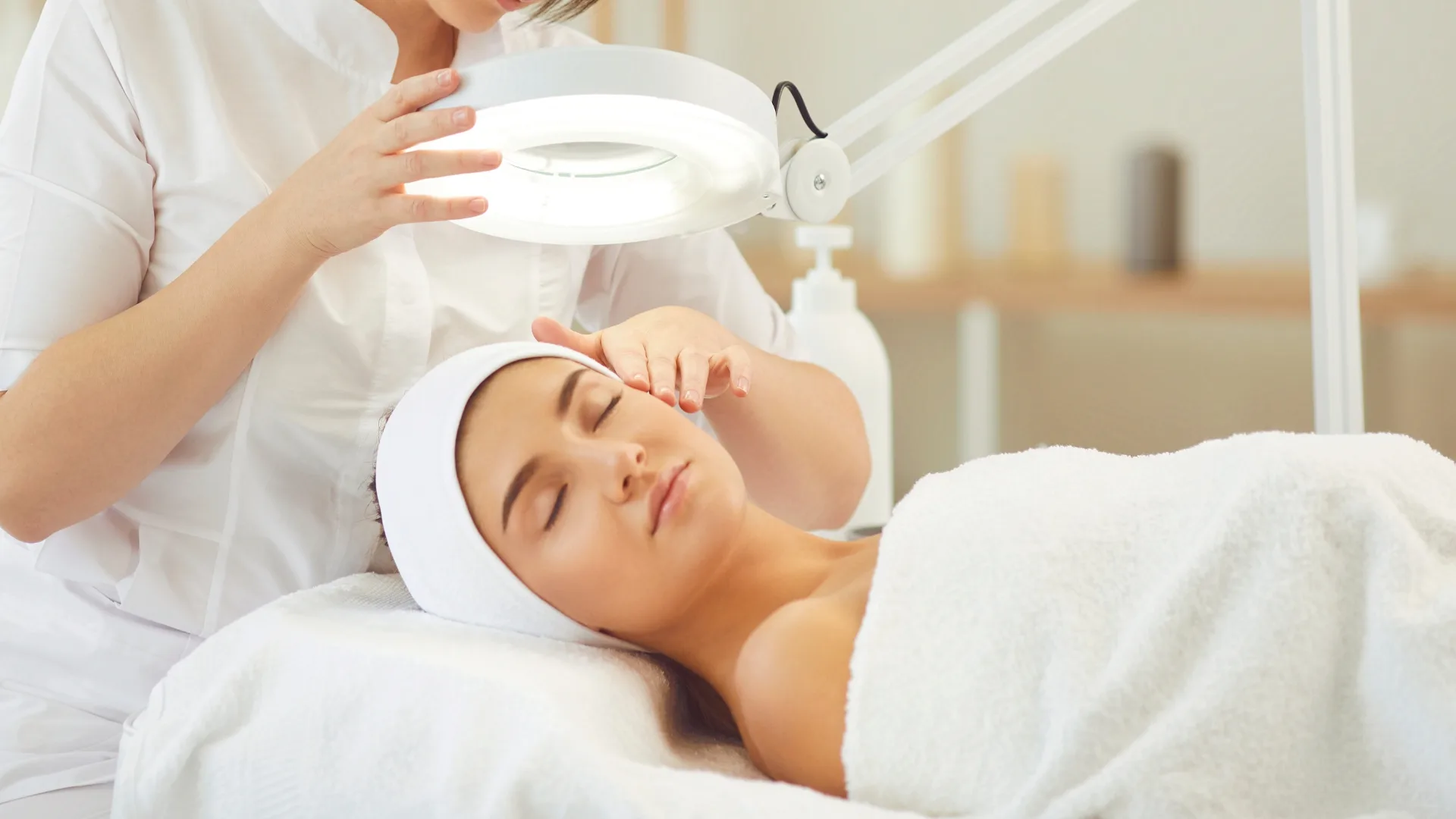 Esthetician performing a facial under a magnifying lamp