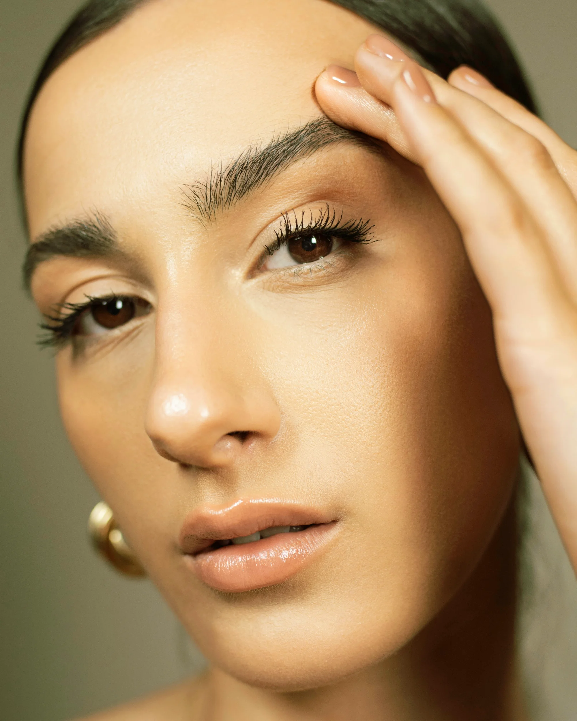 Woman with soft, defined brows touching her cheek