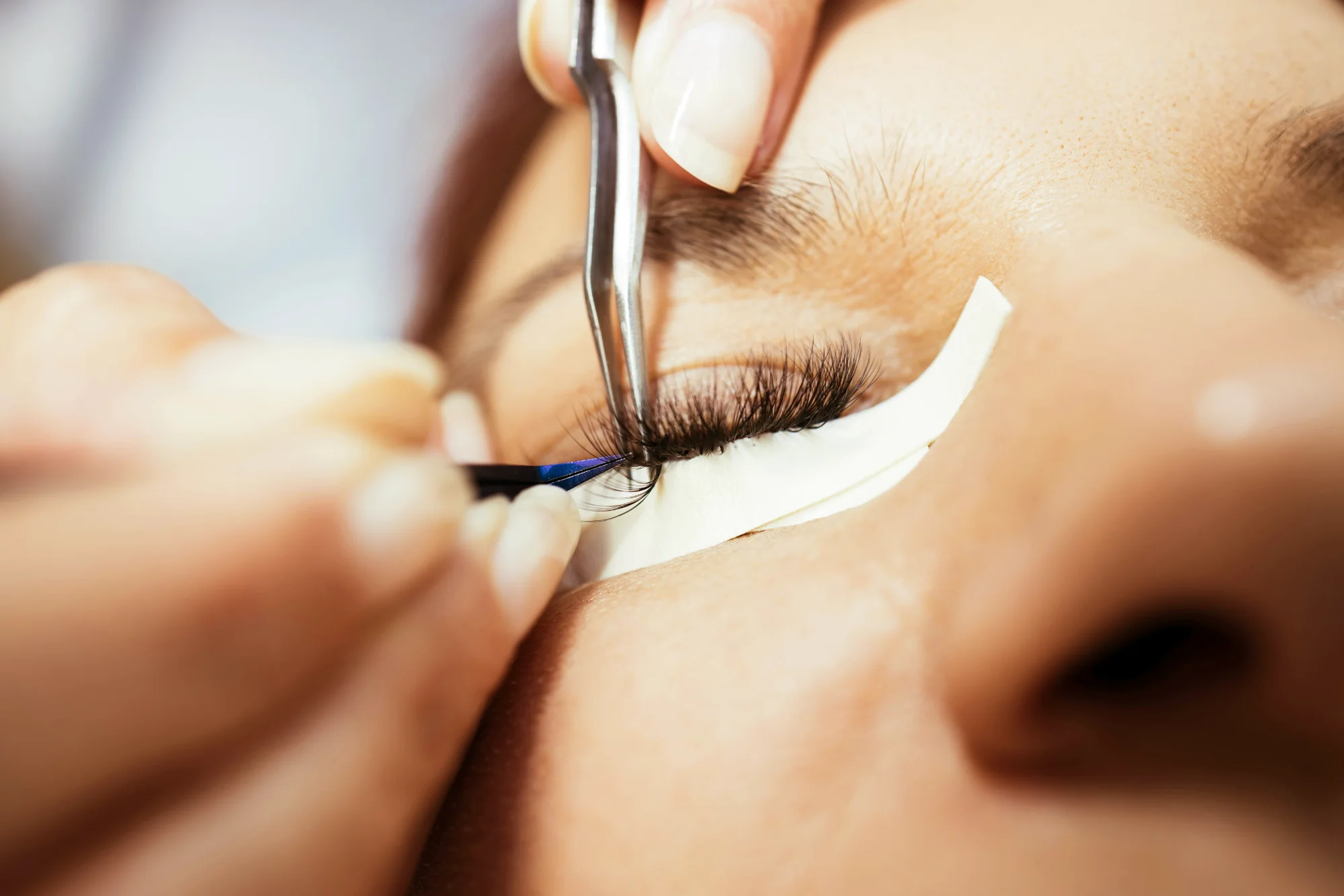 Lash artist placing individual eyelash extensions with fine tweezers