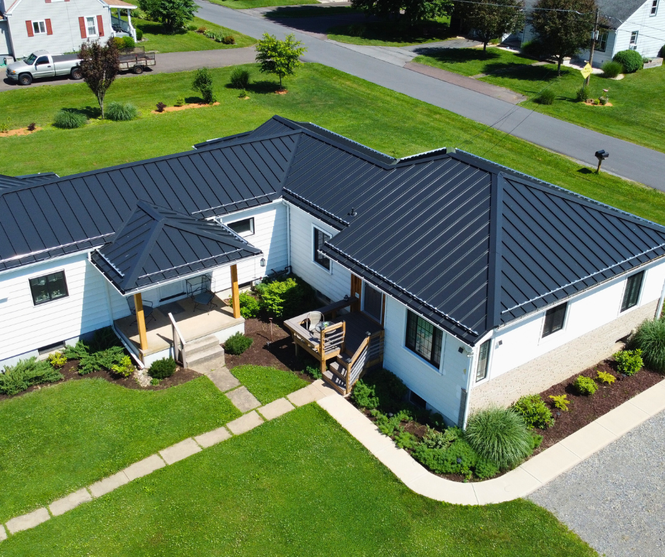 Aerial view of a modern house with a black metal roof, surrounded by green grass and landscaped gardens, emphasizing home aesthetics and outdoor space.