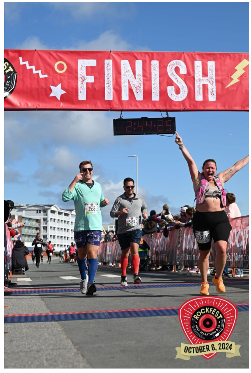 Ace crossing a half marathon finish line with both arms raised