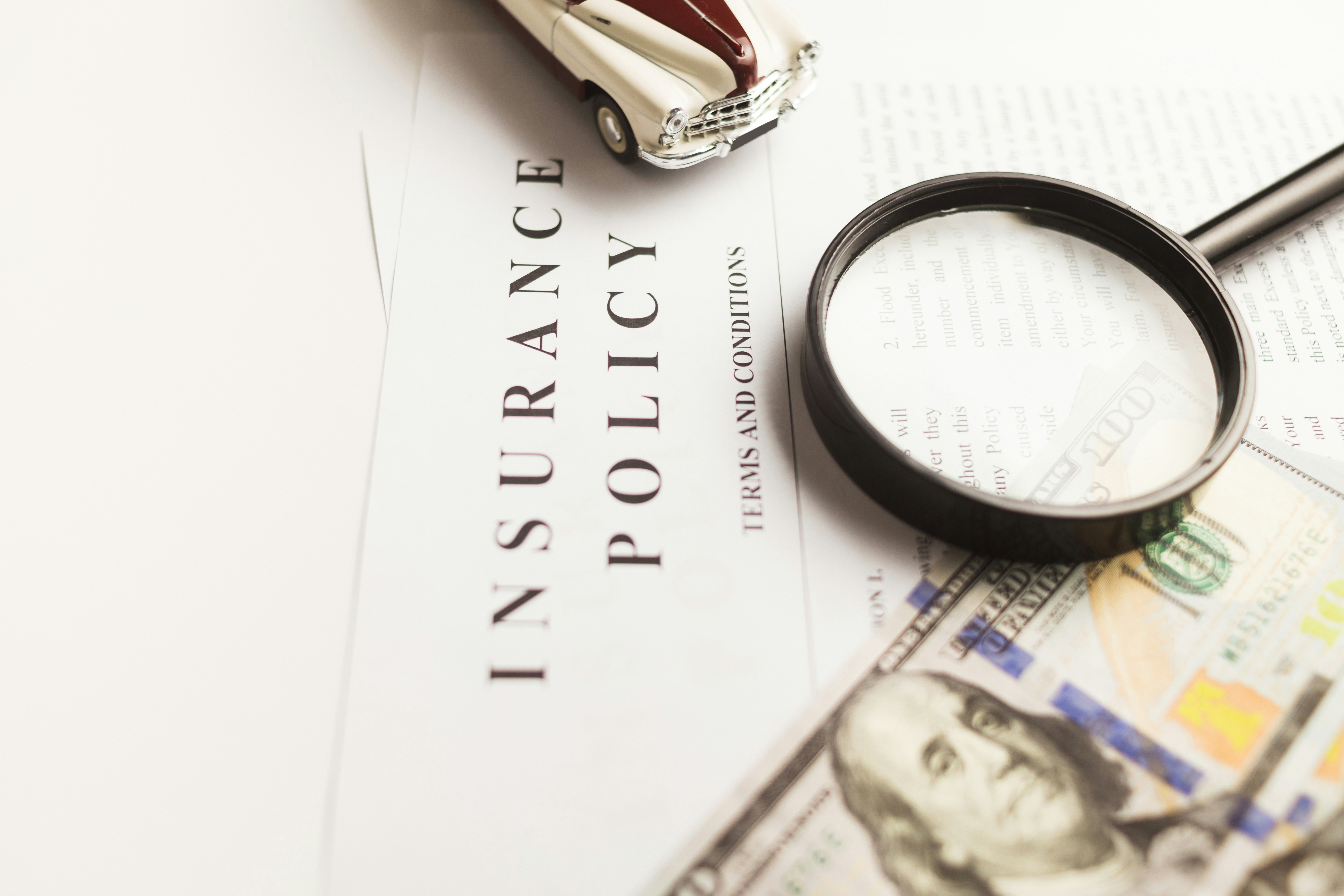 Insurance policy document with magnifying glass and cash, representing travel insurance coverage and costs Insurance policy document with magnifying glass and cash, representing travel insurance coverage and costs