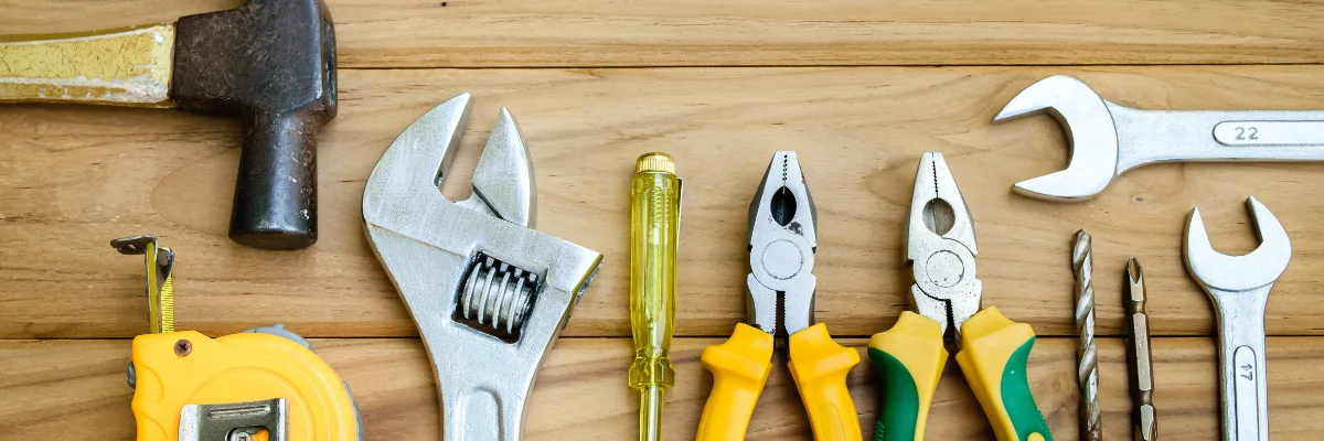 Assorted hand tools including hammer, wrench, and pliers on wooden surface.