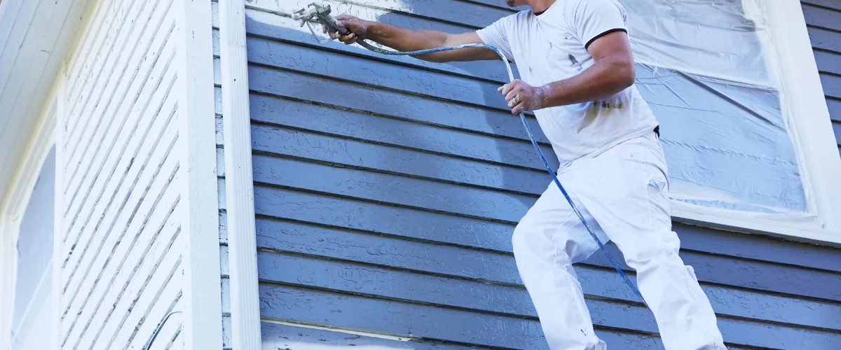 Painter spray painting house exterior siding for renovation project.
