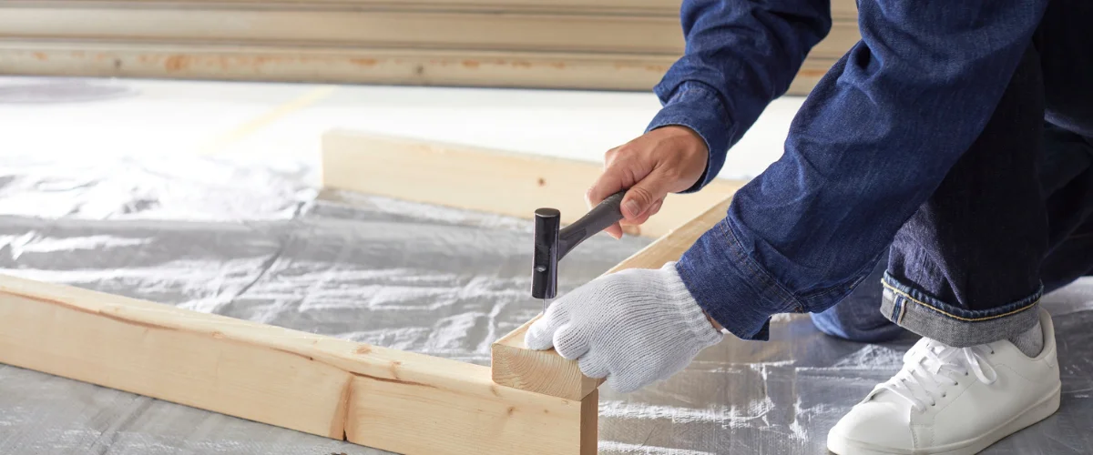 A person in denim clothes and white gloves lightly tapping lumber with a small hammer, building a wooden frame. A person in denim clothes and white gloves lightly tapping lumber with a small hammer, building a wooden frame.